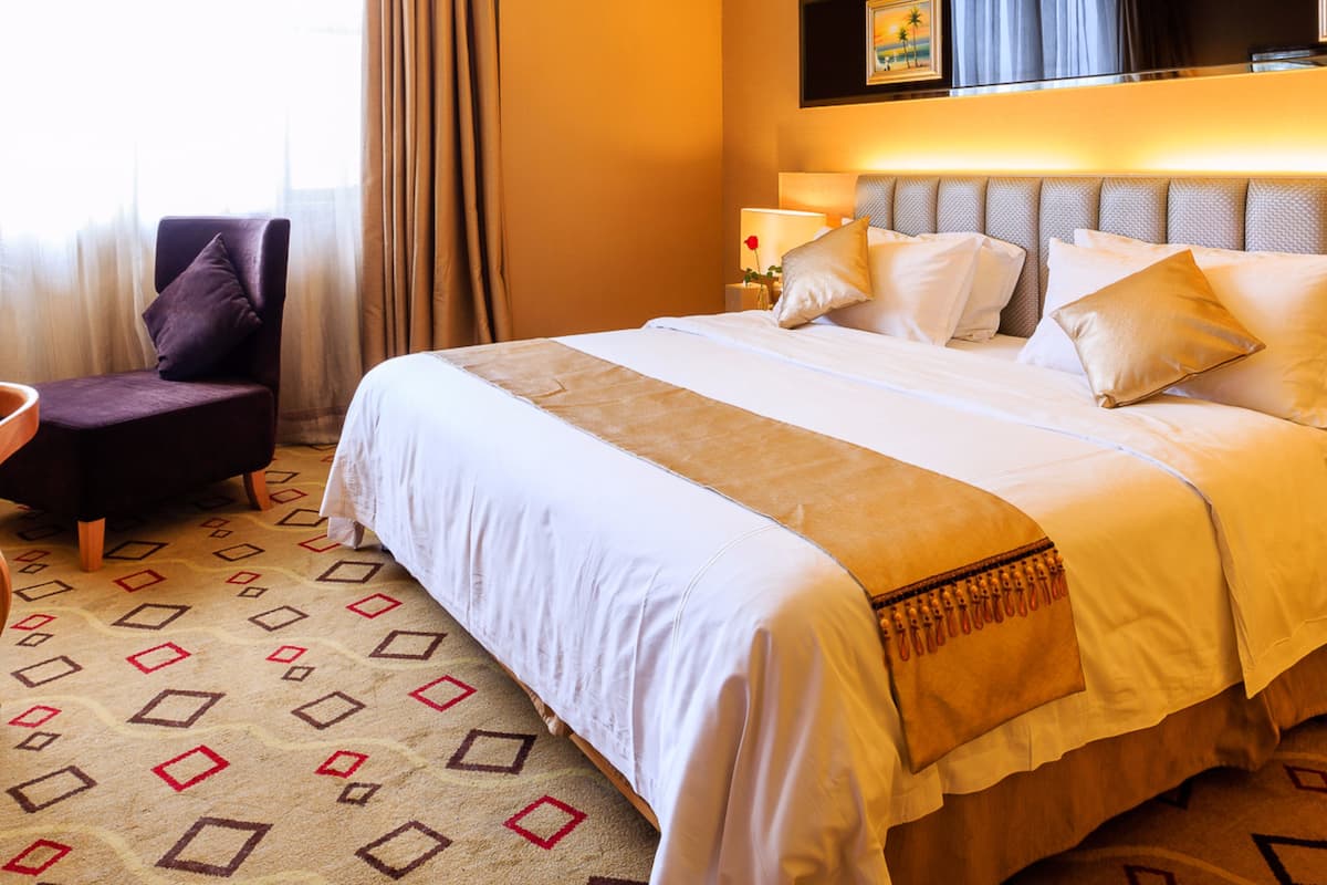 A hotel room with a large bed, a chair, a TV mounted on the wall, and a window with curtains.