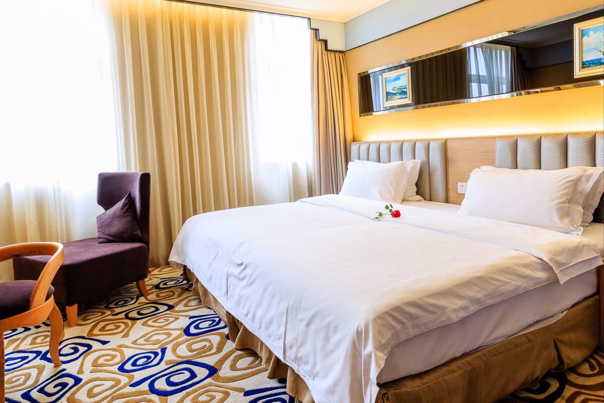 A hotel room with a large bed, a chair, a window with curtains, and a patterned carpet.
