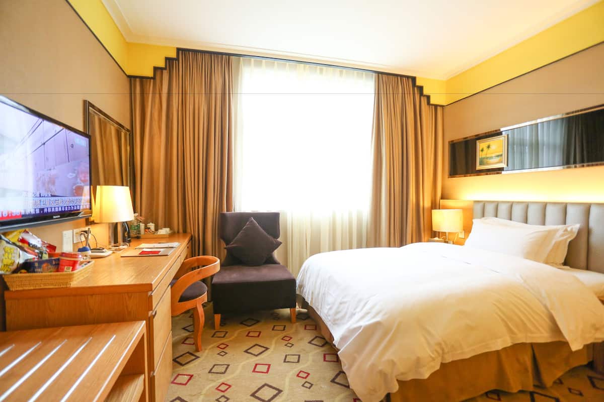 A hotel room with a bed, desk, chair, television, and curtains.