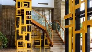 A spacious lobby with a polished wooden floor, a central staircase with glass railings, and a yellow geometric wall structure. - Vilu Reef International Hotel (Zigong)