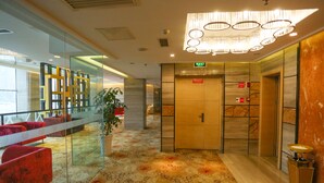 A hotel lobby with a patterned carpet, red seating, a glass partition, and a chandelier. - Vilu Reef International Hotel (Zigong)