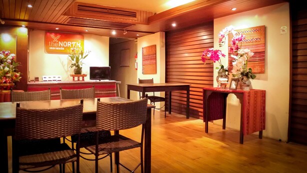 A restaurant with wooden furniture, a reception desk, and decorative flowers. - The North Hotel (Chiang Rai)