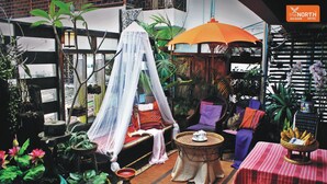 A cozy indoor setting with a bed under a white canopy, a wicker table with a teapot, and a variety of plants and furniture. - The North Hotel (Chiang Rai)