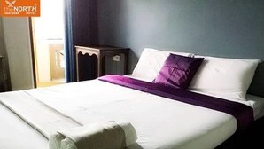A hotel room with a neatly made bed, a bedside table, and a window with curtains. - The North Hotel (Chiang Rai)