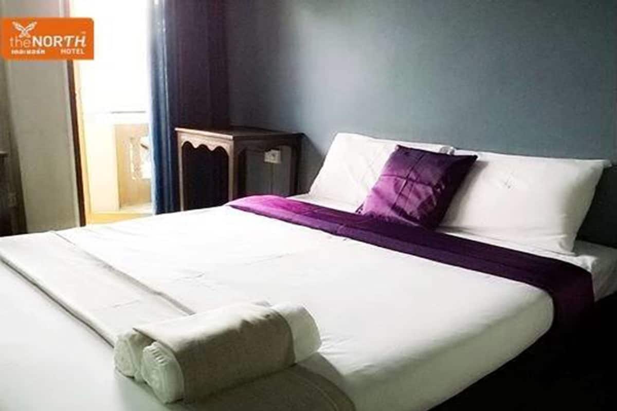 A hotel room with a neatly made bed, a bedside table, and a window with curtains.
