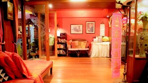A cozy room with a wooden floor, a red sofa, a bookshelf, and a table with a white tablecloth. - The North Hotel (Chiang Rai)