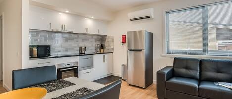 Una cocina moderna con armarios blancos, un refrigerador de acero inoxidable y un comedor con un tazón amarillo y sillas negras.