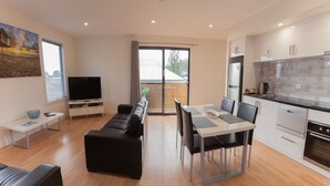 Un salon moderne comprenant un canapé, un téléviseur et un coin repas avec des chaises et une table.