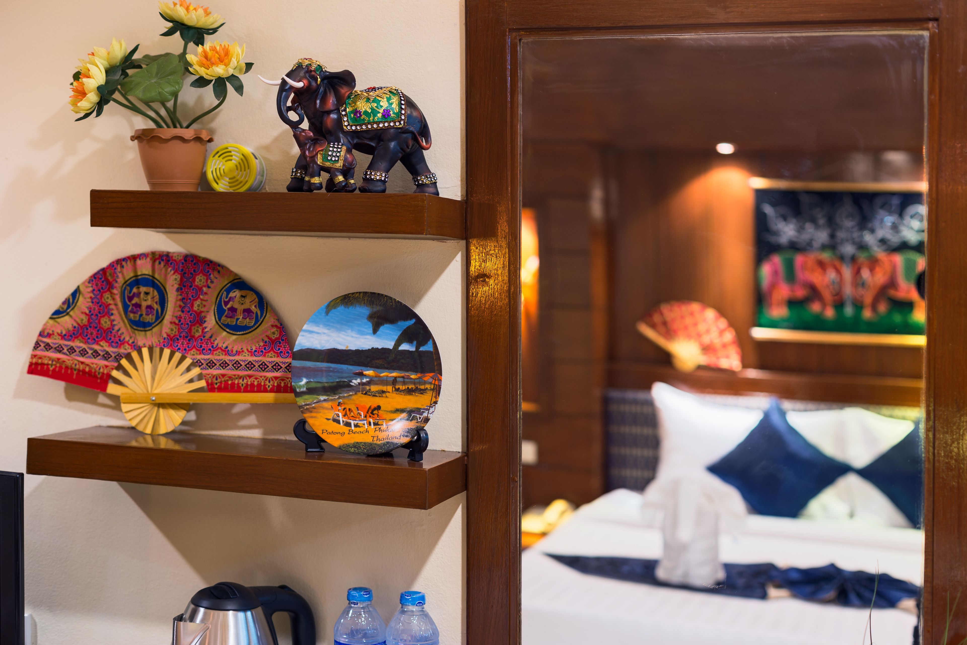 A hotel room with a wooden shelf displaying decorative items, a bed with blue and white bedding, and a large painting on the wall.