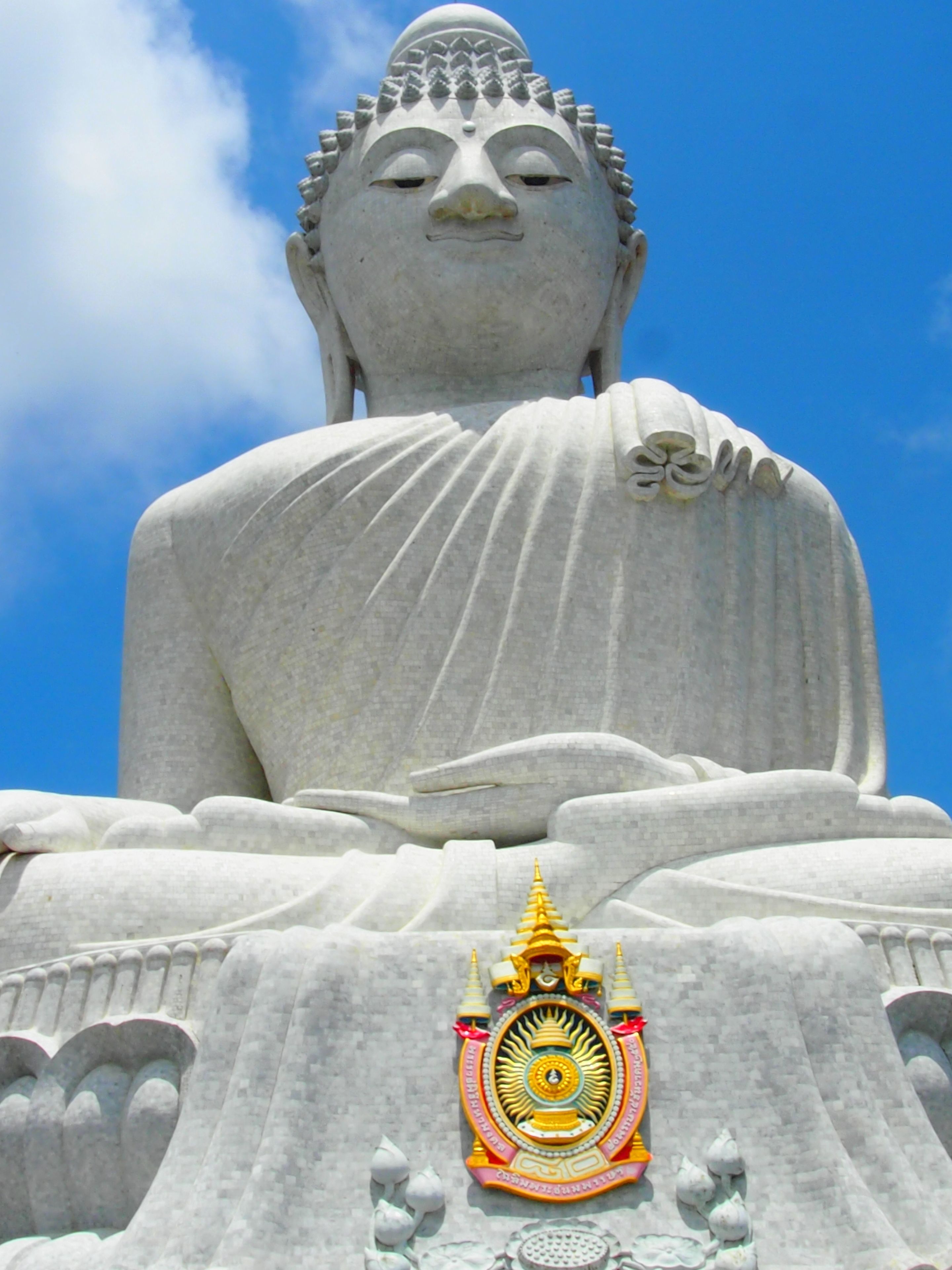 Eine große Buddha-Statue aus Stein mit aufwendigen Schnitzereien und einem goldenen Emblem am Fuß.