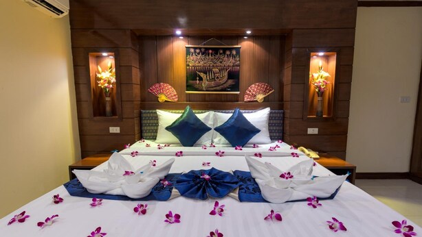 A hotel room with a large bed, decorative pillows, wall-mounted fans, and a painting above the bed. - P R Patong Hotel (Patong)