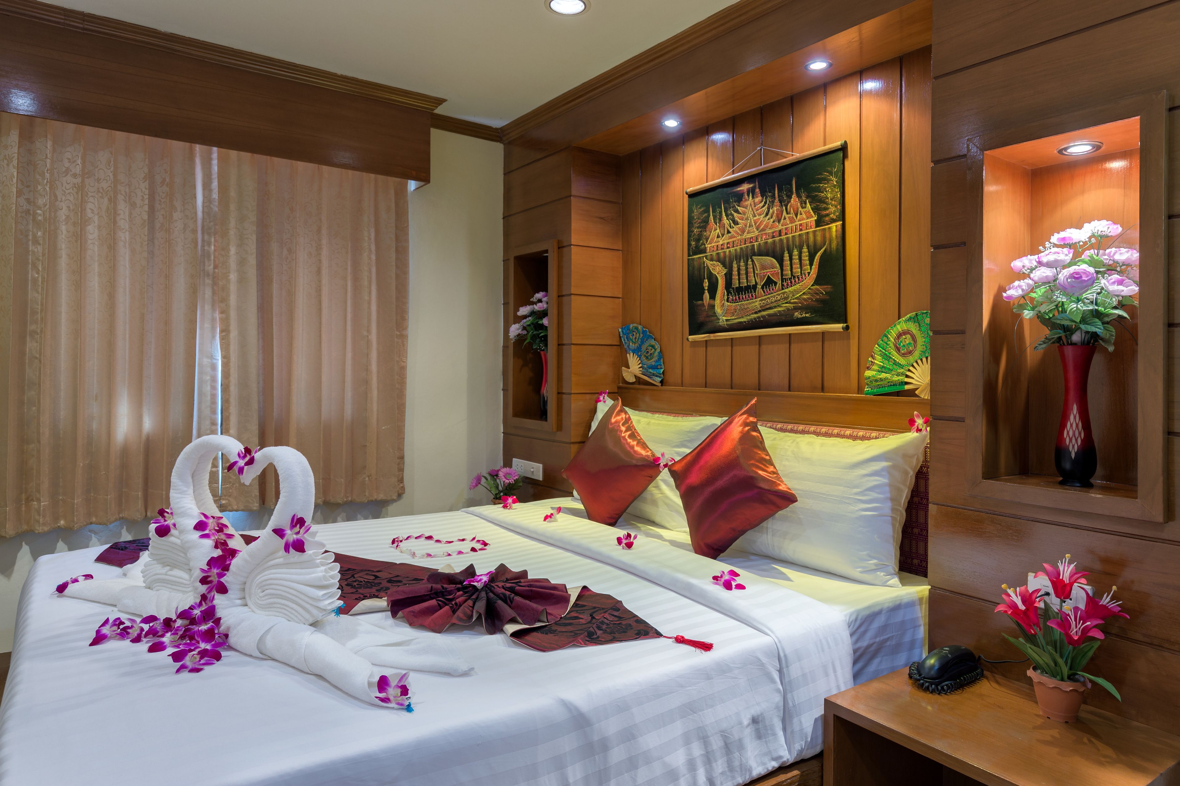Habitación de hotel elegante con una cama grande, almohadas decorativas, cabecera de madera y una obra de arte enmarcada que muestra una escena tradicional.