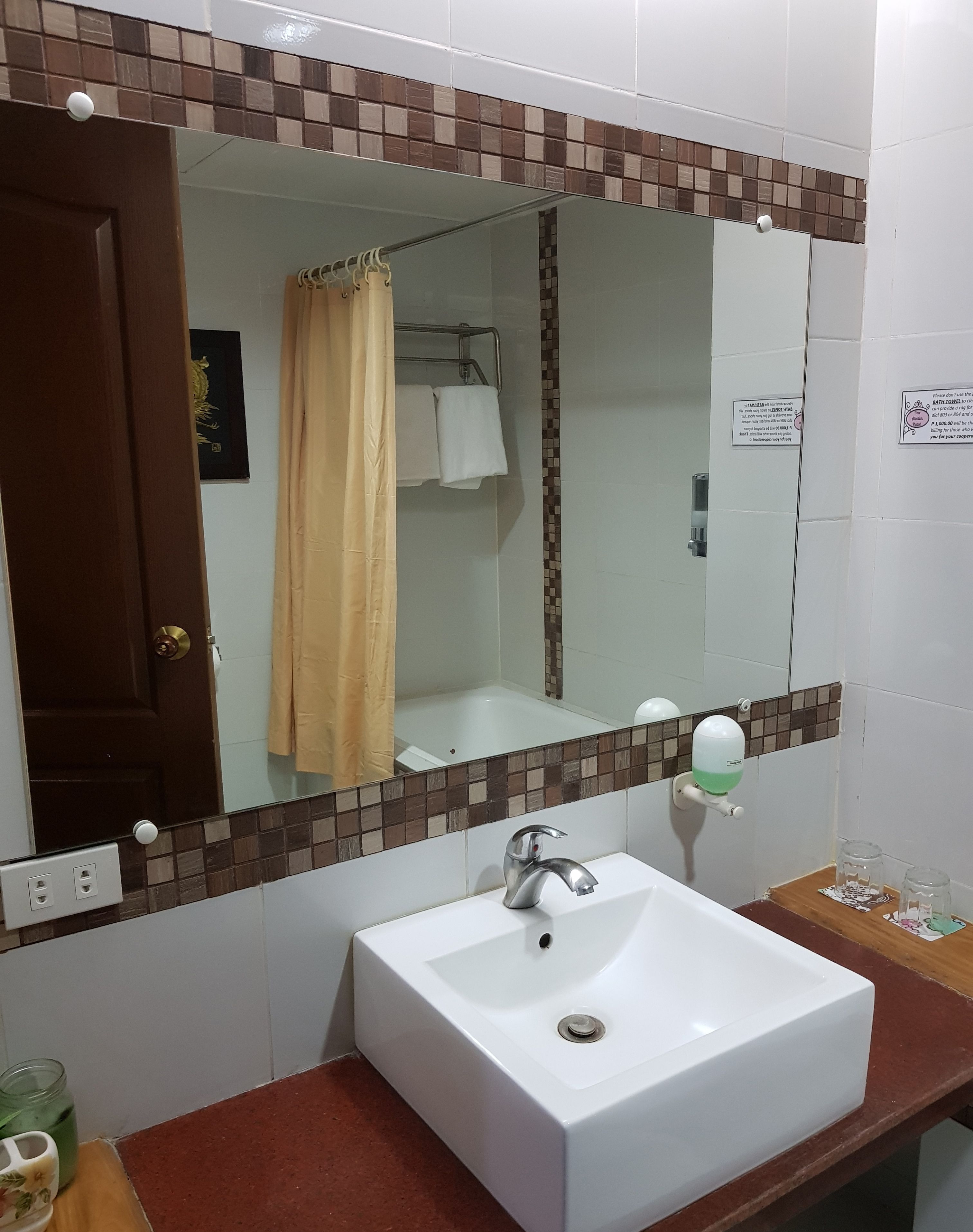 Une salle de bain avec un lavabo blanc, un miroir, un rideau de douche et un distributeur de savon.