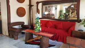 Una sala de estar acogedora con un sofá rojo, sillas de madera, una mesa de centro de vidrio y un árbol de Navidad.