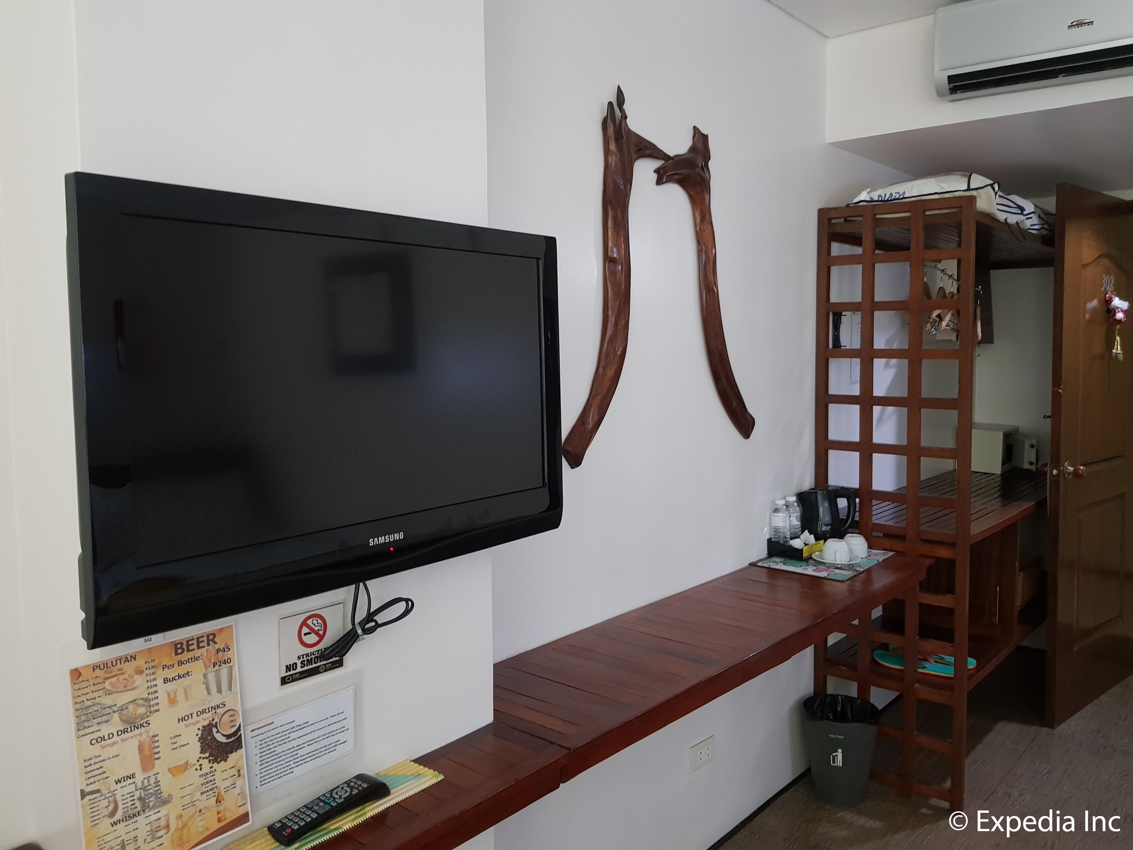 A hotel room with a flat-screen TV mounted on the wall, a wooden bench with a tray, and a wooden shelf with a ladder.