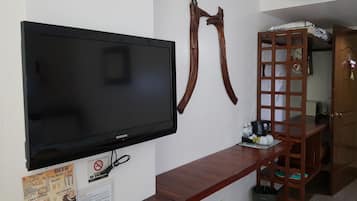 A hotel room with a flat-screen TV mounted on the wall, a wooden bench with a tray, and a wooden shelf with a ladder.