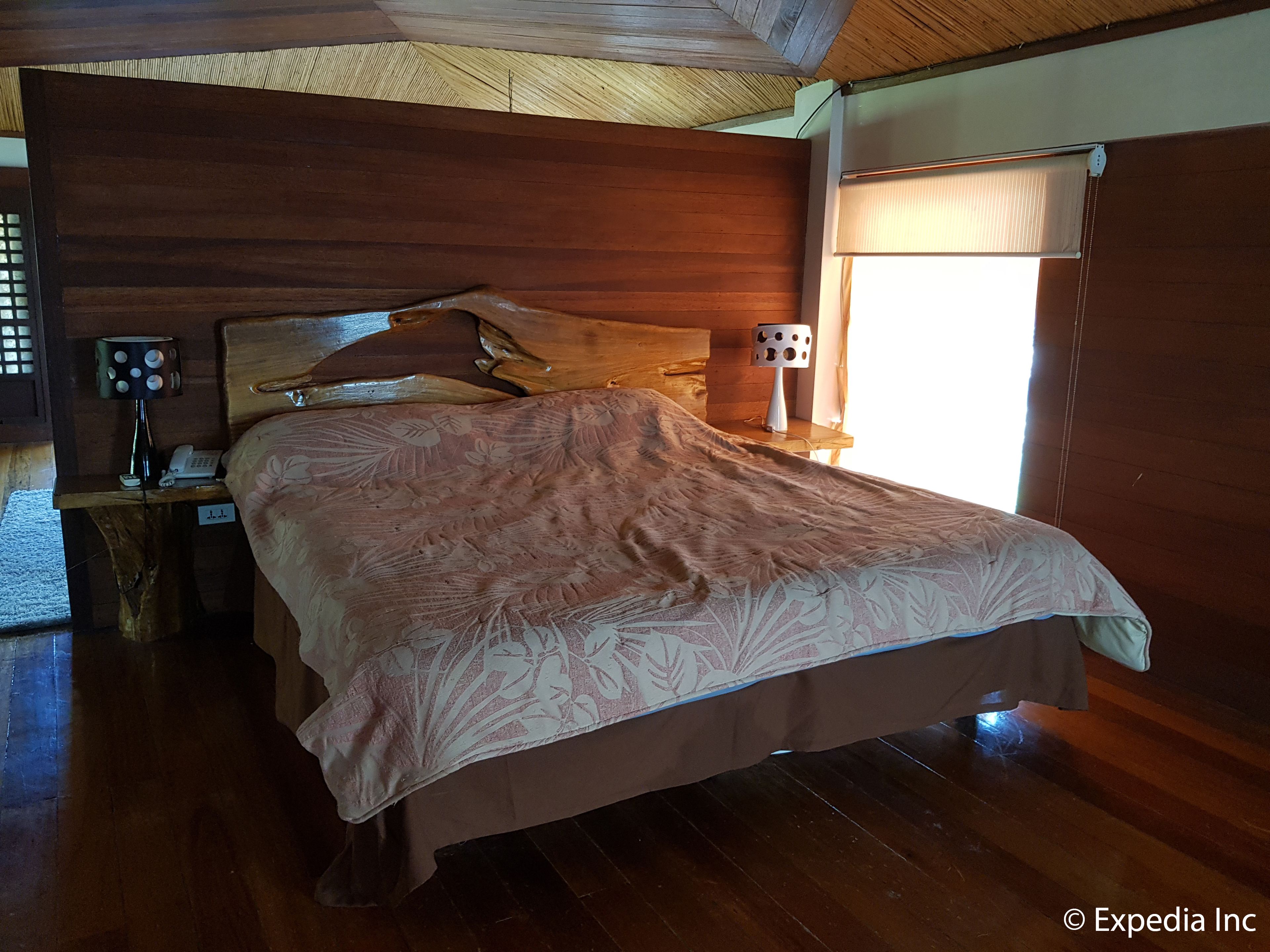 Un lit en bois, recouvert d’une couvre-lit à motifs floraux, dans une pièce dont les murs et le plancher sont également en bois.