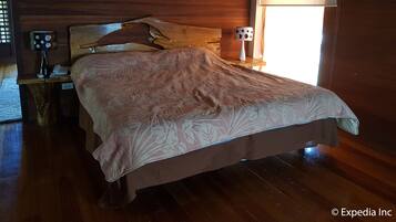 Un lit en bois, recouvert d’une couvre-lit à motifs floraux, dans une pièce dont les murs et le plancher sont également en bois.