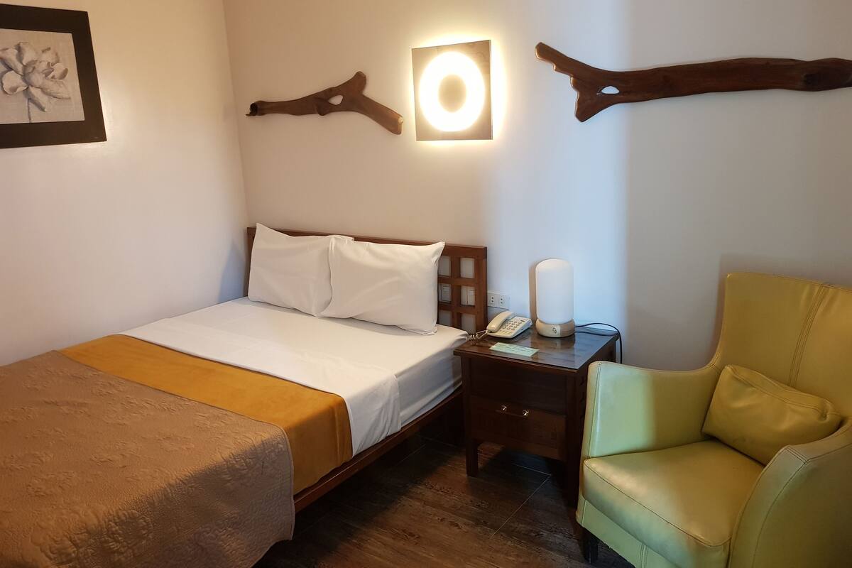 A hotel room with a bed, bedside table with a lamp, a chair, and wall decor.