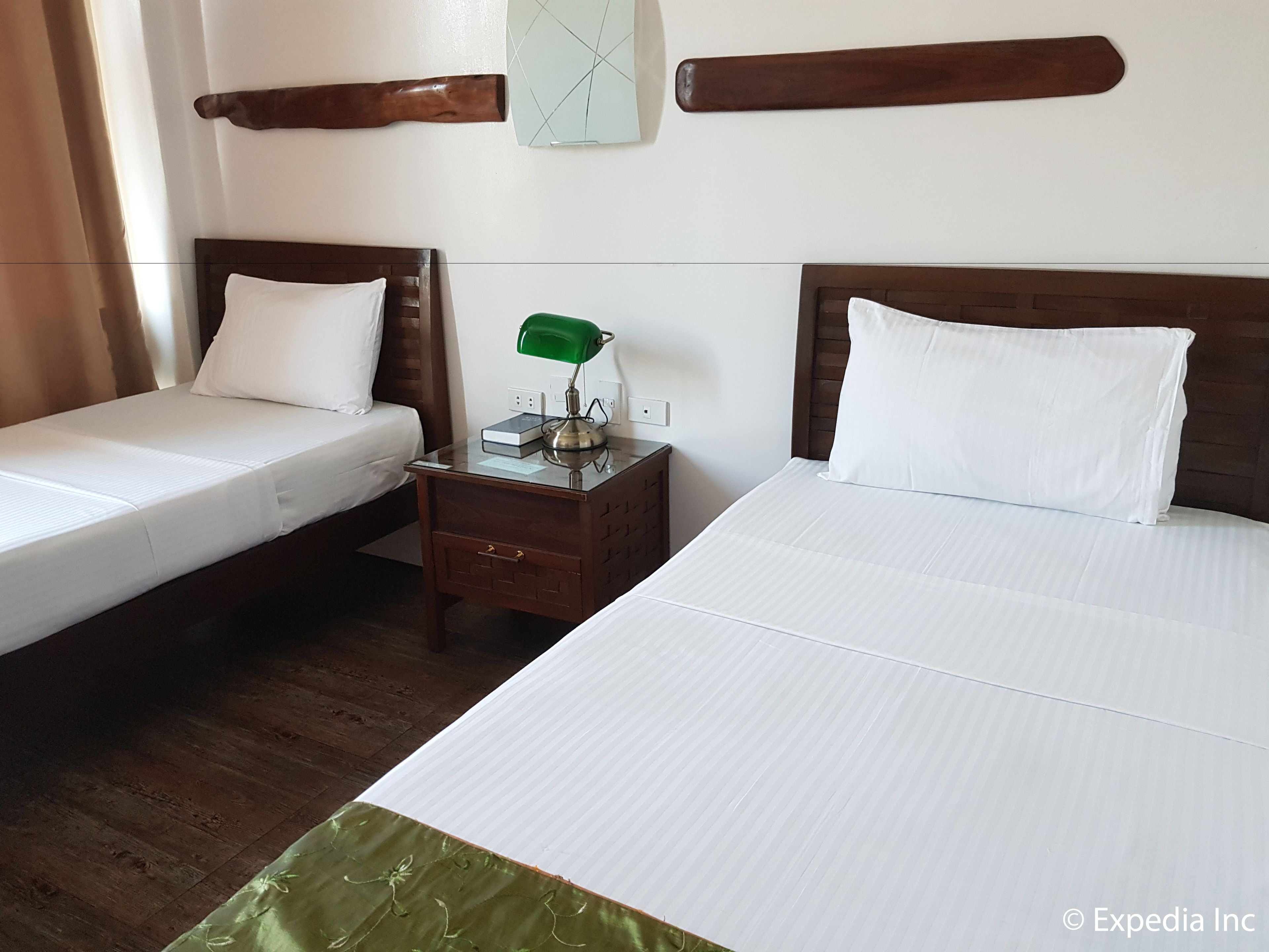 A hotel room with two single beds, a nightstand with a green lamp, and a wall clock.