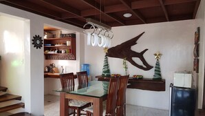 Un comedor con una mesa de vidrio, sillas de madera, un dispensador de agua y un árbol de Navidad.