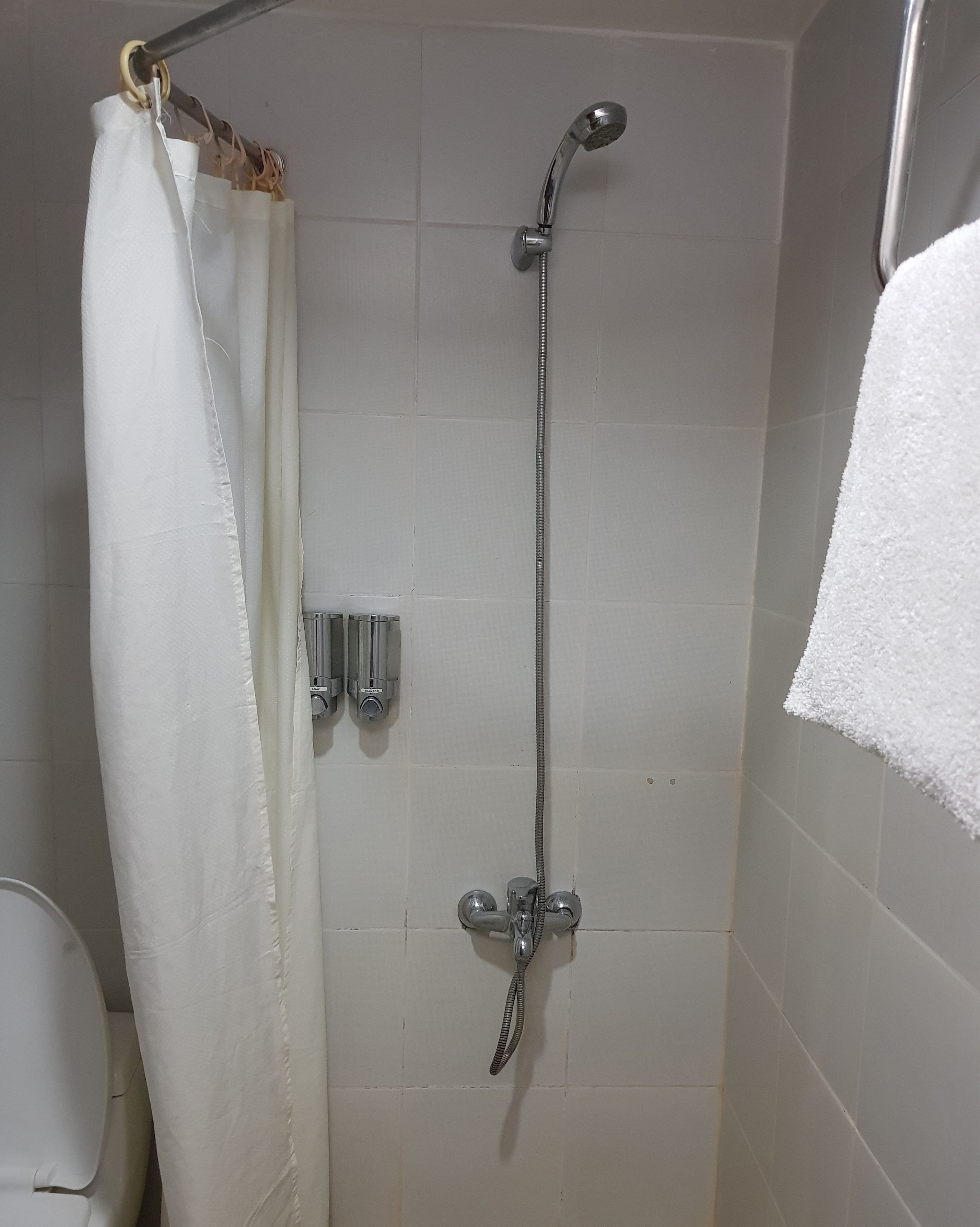 Zona de ducha con alcachofa, cortina y barra para toallas.
