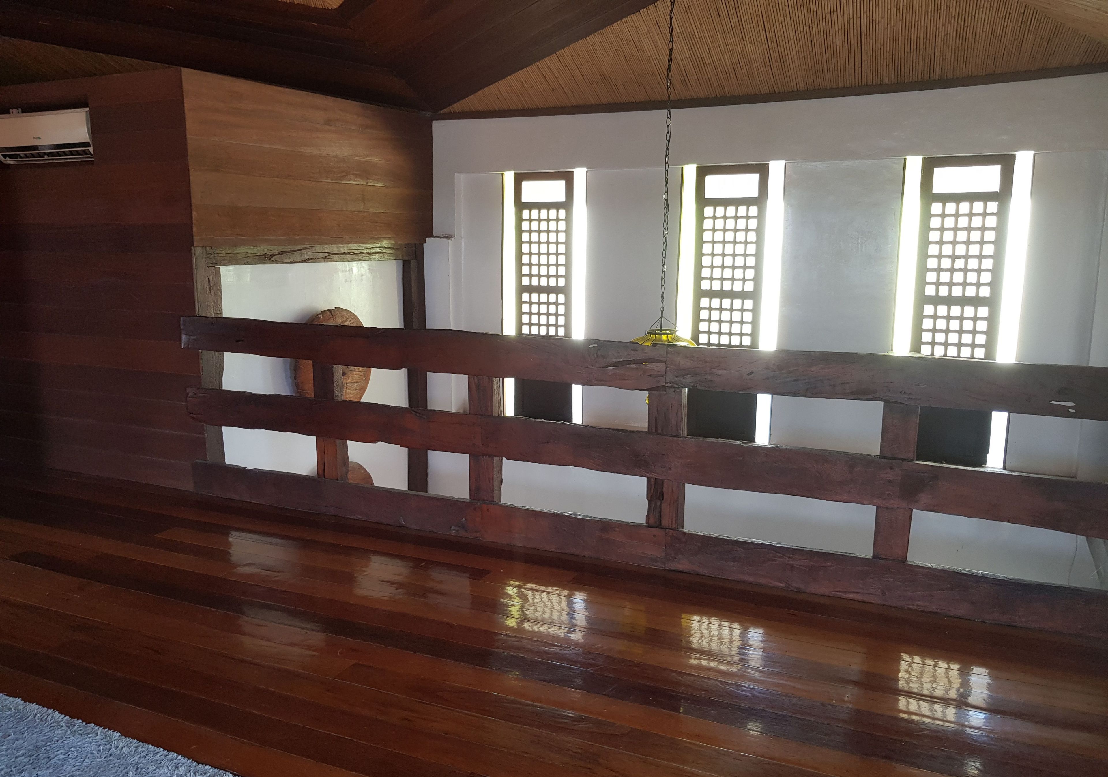 Una stanza con pavimento in legno, ringhiera di legno e finestre con inferriate.