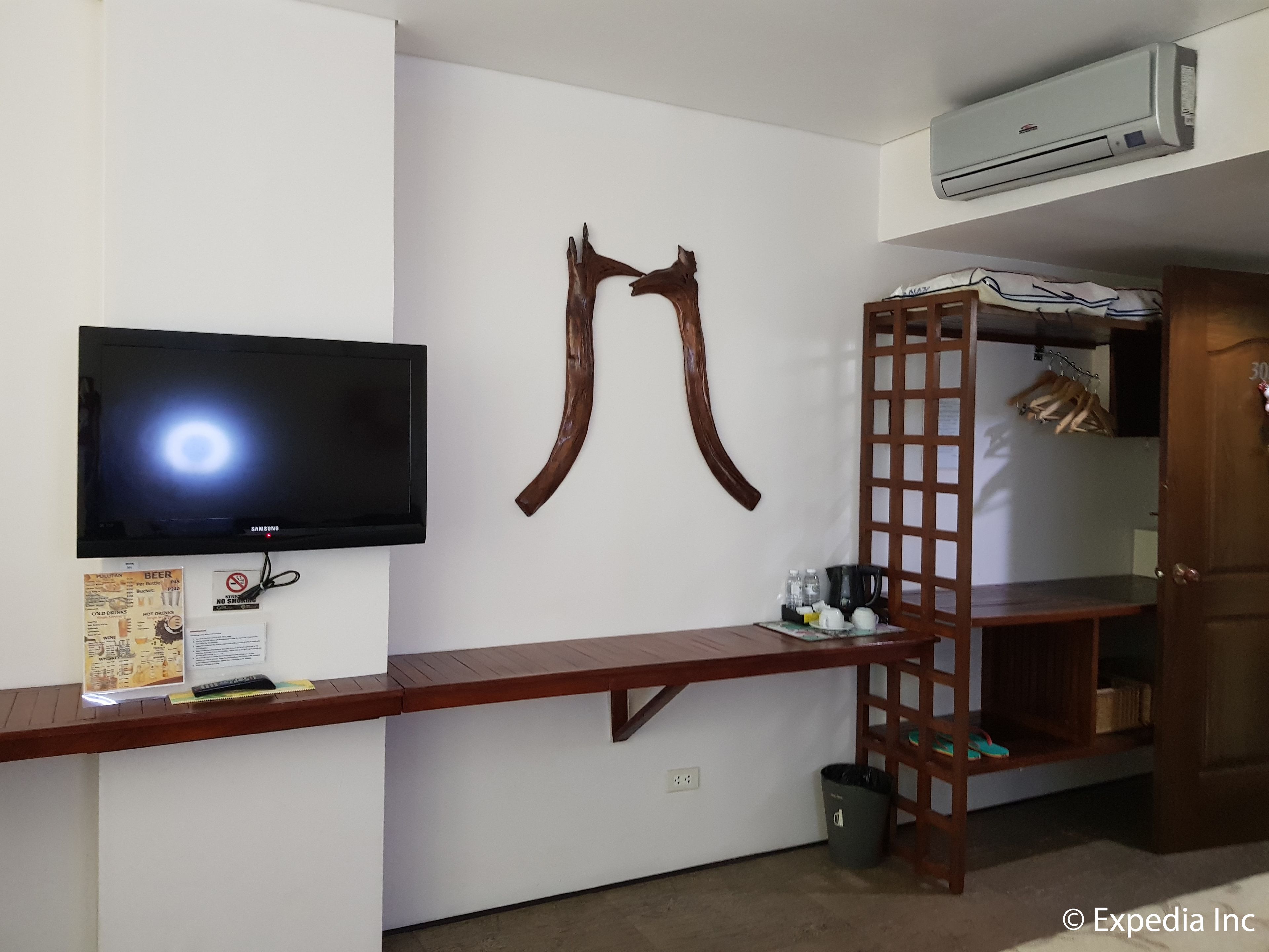 A room with a mounted TV, a wooden shelf with a ladder, a coat rack, and an air conditioning unit.