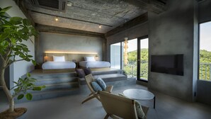 A modern bedroom with a large bed, a sofa, and a TV. There are steps leading to a balcony with a view of greenery.