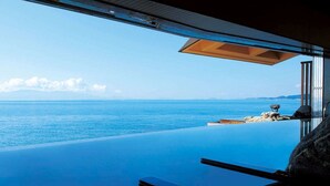 A room with a large window overlooking a clear blue sea and a rocky shoreline.