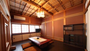 Una habitación japonesa tradicional con suelo de tatami, una mesa de madera baja, cojines, un televisor y una puerta corredera.