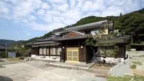 Una casa tradicional japonesa con tejado de baldosas, paredes de madera y un jardín delantero.