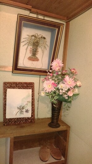 Un tableau encadré représentant un homard est accroché au mur, un vase rempli de fleurs roses est posé sur une étagère en bois, et une paire de pantoufles se trouve en dessous.