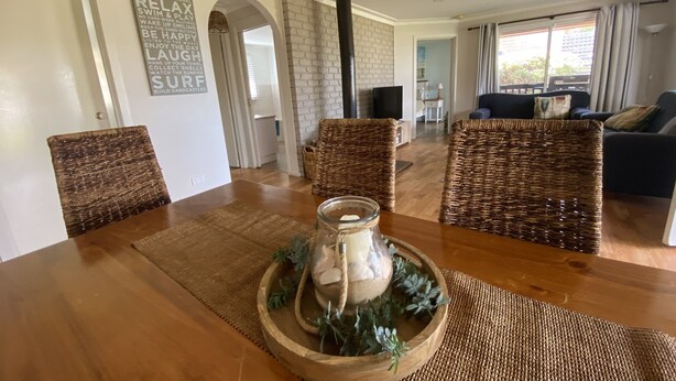 A dining area with a wooden table, wicker chairs, and a decorative centerpiece. - 90 Mile Beach House & Villas (Golden Beach)