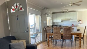 A living room with a sofa, a dining table with chairs, a kitchen area, and a balcony. - 90 Mile Beach House & Villas (Golden Beach)