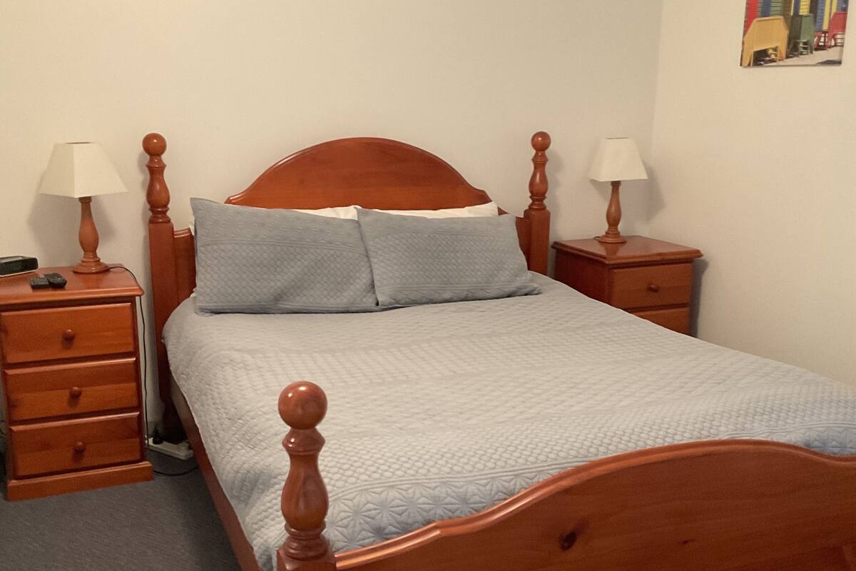 Ein hölzernes Bett mit Kopfteil, zwei Nachttische mit Lampen und ein Bild an der Wand.