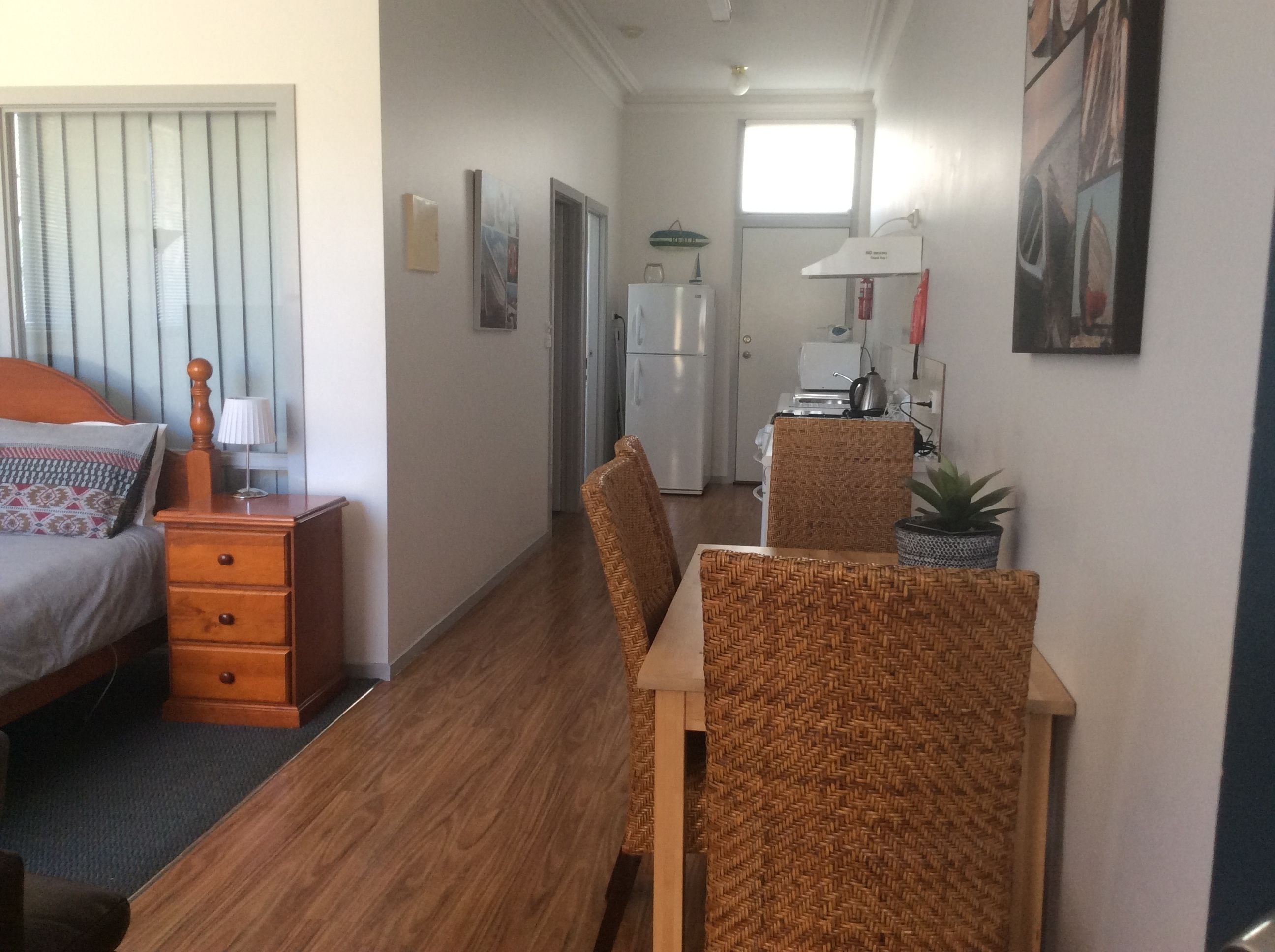 A compact hotel room with a bed, wooden nightstand, and a dining area with wicker chairs and a table.