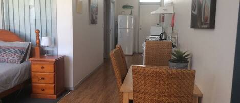 A compact hotel room with a bed, wooden nightstand, and a dining area with wicker chairs and a table.