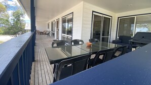A covered outdoor patio with a glass table and chairs, a barbecue grill, and a view of the beach. - 90 Mile Beach House & Villas (Golden Beach)