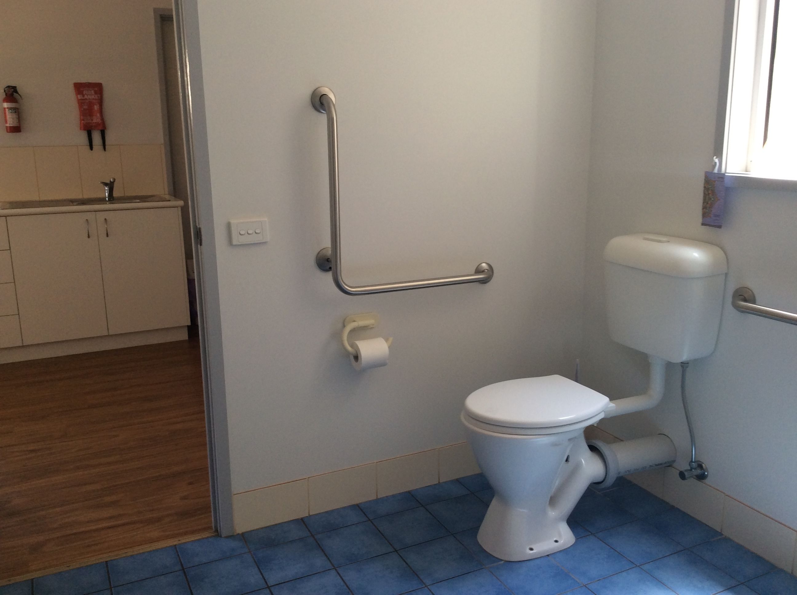 Ein Badezimmer mit Toilette, blauem Fliesenboden und einer Haltestange zur Barrierefreiheit.
