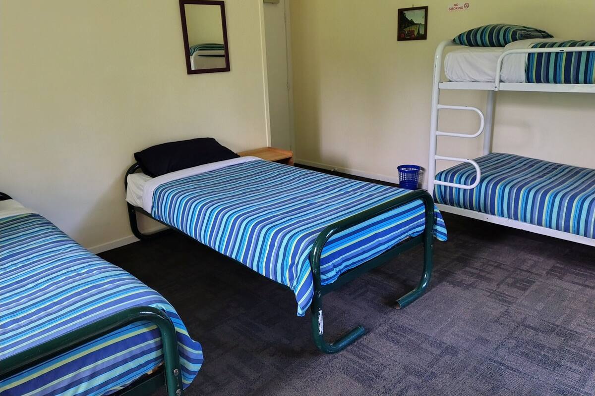 A room with three bunk beds, each with a striped blue and white bedspread. There is a small blue basket on the floor near one bed.