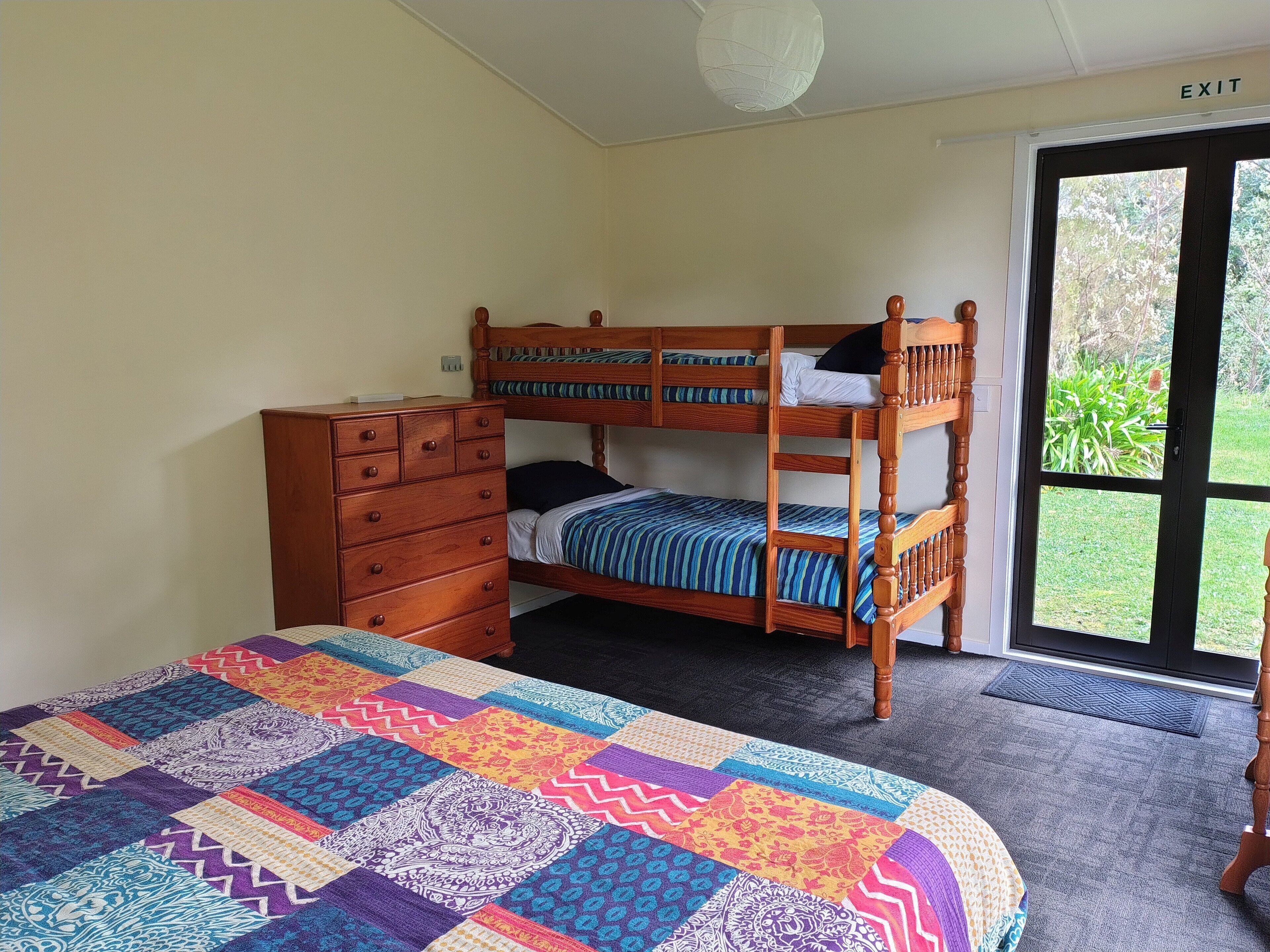 A bedroom with a bunk bed, a wooden dresser, a colorful quilt, and a view of the outdoors through a glass door.