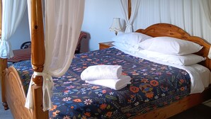 Una cama con dosel adornada con cortinas blancas, una colcha estampada con motivos florales y una toalla blanca doblada con cuidado.