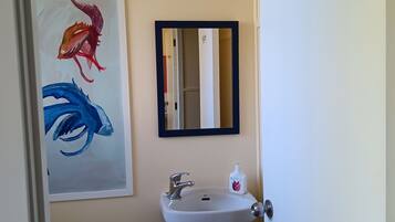 Un baño con lavamanos, espejo e inodoro. Hay un cuadro de un pez en la pared.