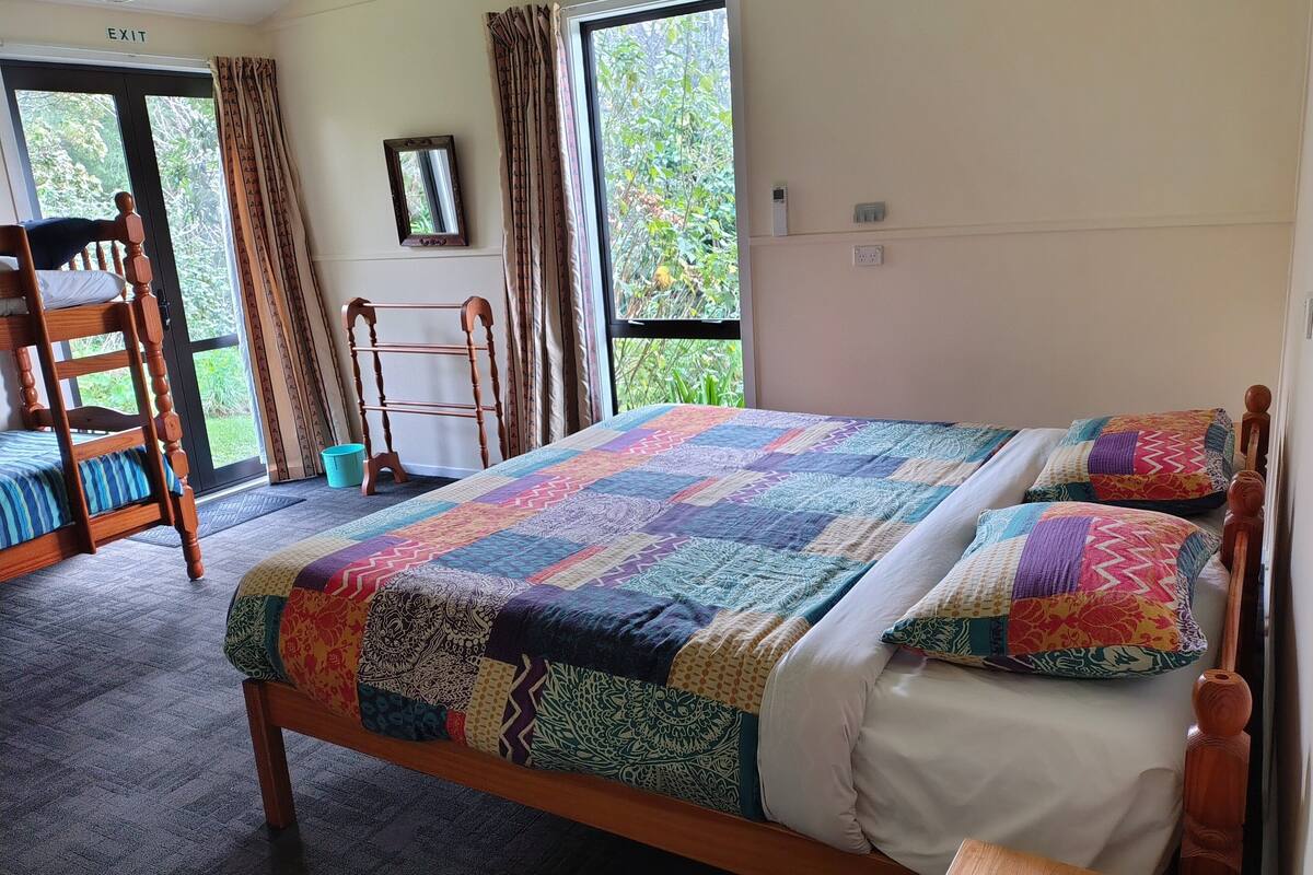 A bedroom with a large bed, a wooden chair, a ladder, and a window with curtains.