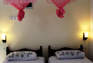 Dos camas con almohadones estampados, una lámpara fijada a la pared y un dosel decorativo.