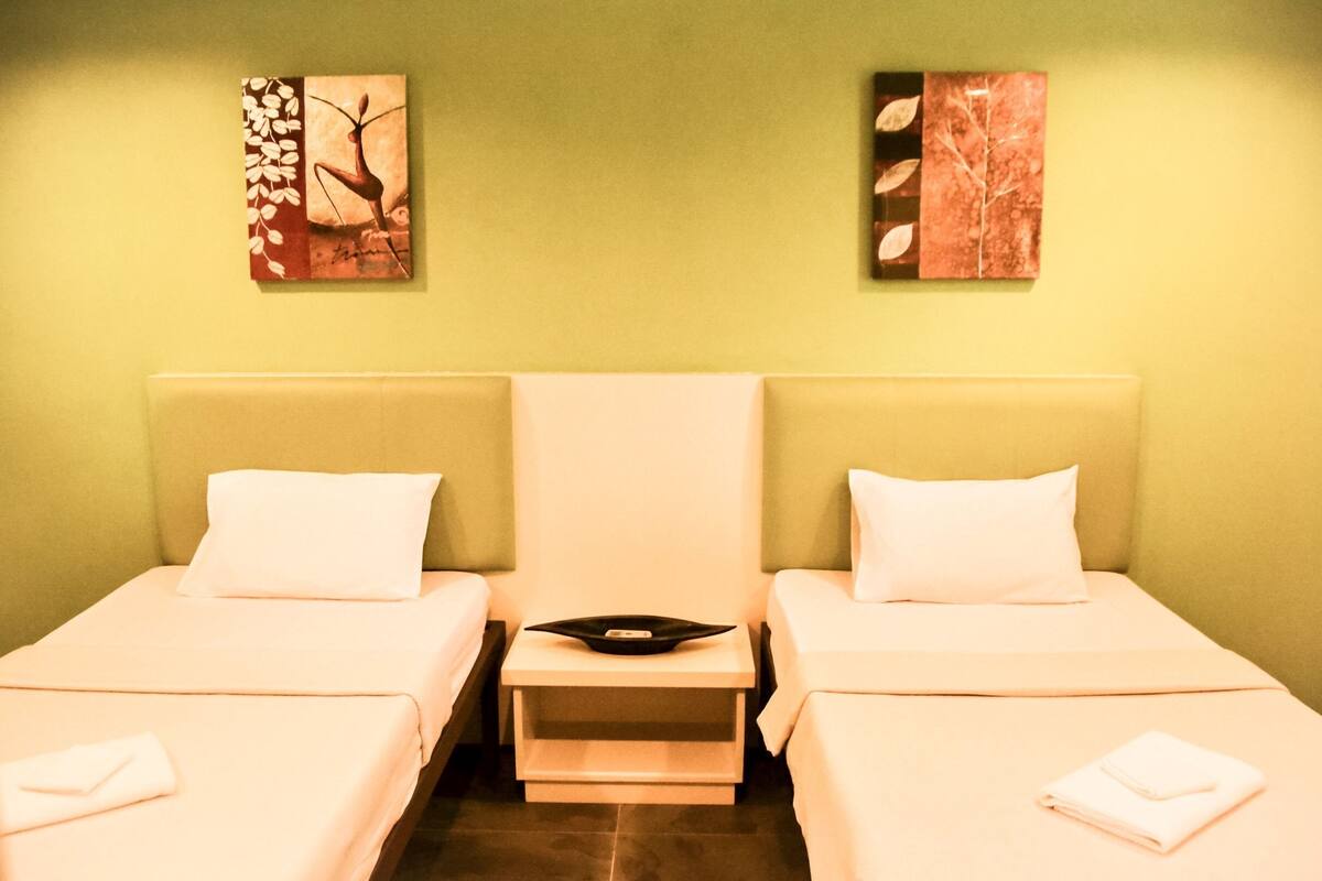 A hotel room with two beds, a nightstand, and artwork on the walls.