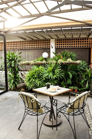 An outdoor patio with a table and chairs, surrounded by lush green plants and a wooden fence. - Qi Hotel and Club (Kota Kinabalu)