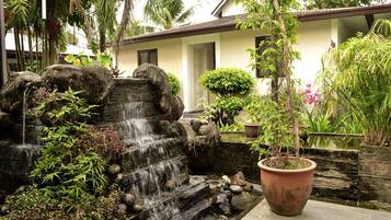 A waterfall feature with surrounding greenery, a potted plant, and a building with a white facade and windows.