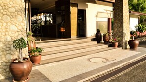 A hotel entrance with stone walls, large potted plants, and a tiled entrance area. - Qi Hotel and Club (Kota Kinabalu)